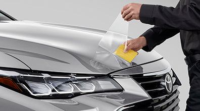 Person applying a car wrap film to a Toyota vehicle's front