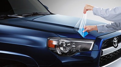 Professional dealer-installed paint protection film being applied on the hood of a blue Toyota vehicle to prevent scratches and damage