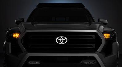 Illuminated Front Emblem glowing on black Toyota truck grille at night
