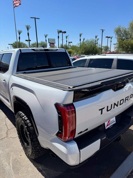 White Toyota Tundra truck with installed Tri-Fold Hard Tonneau Cover on the bed for secure, weather-resistant protection.